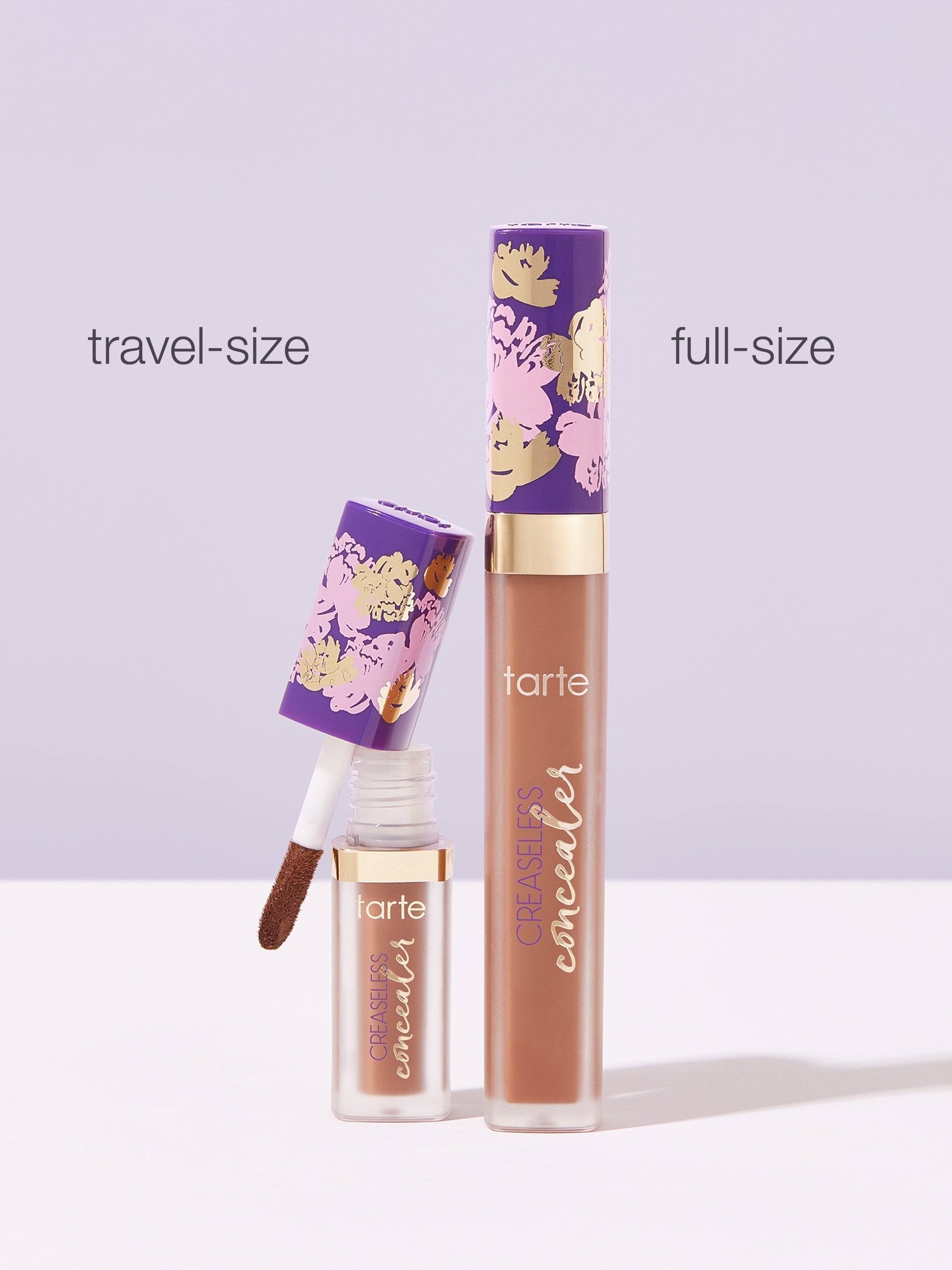 Two Tarte Cosmetics concealers, one travel-size and one full-size, stand against a light purple background. The smaller one is open, displaying the applicator; both tubes have floral designs. Text: travel-size, full-size, tarte, CREASELESS concealer.