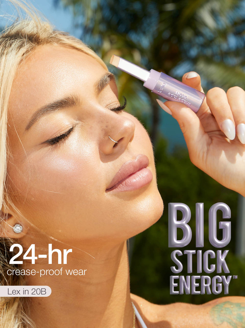 Woman applying makeup with a product labeled 'Big Stick Energy' outdoors.