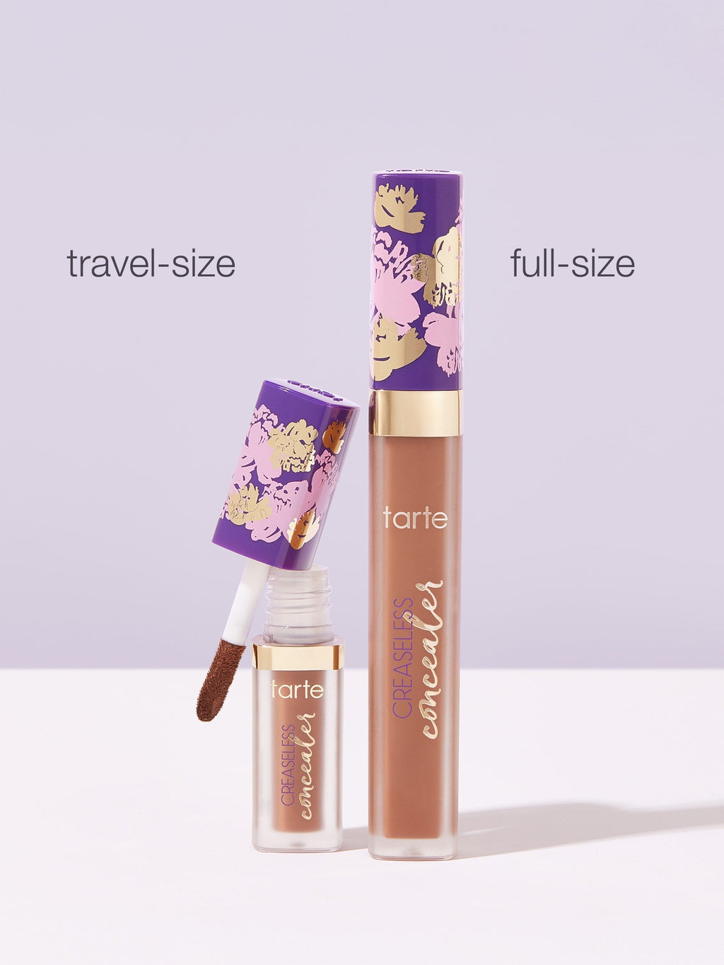 Two Tarte Cosmetics concealers, labeled travel-size and full-size, stand on a light surface. The travel-size concealer's applicator is visible. Both containers feature a purple floral design.