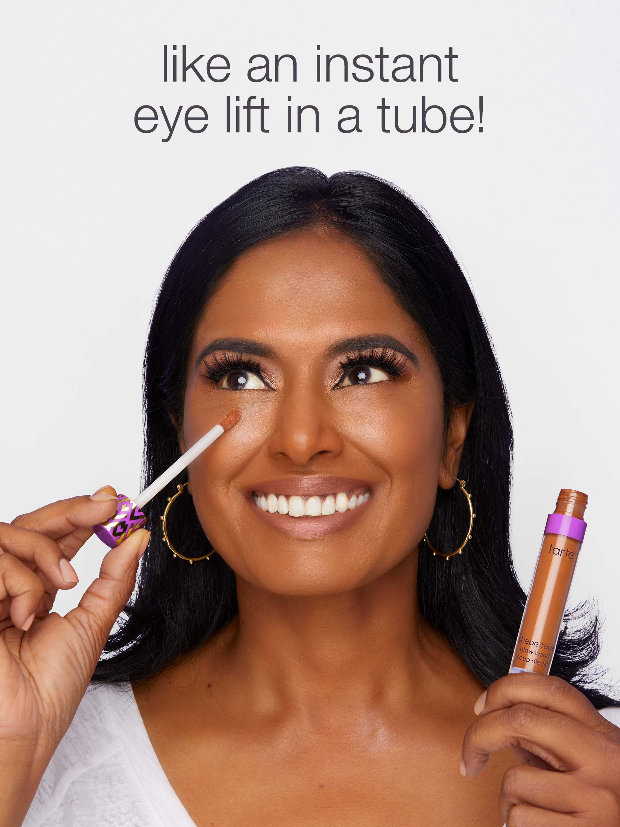 Woman applying makeup with a product labeled 'like an instant eye lift in a tube!' on a plain background