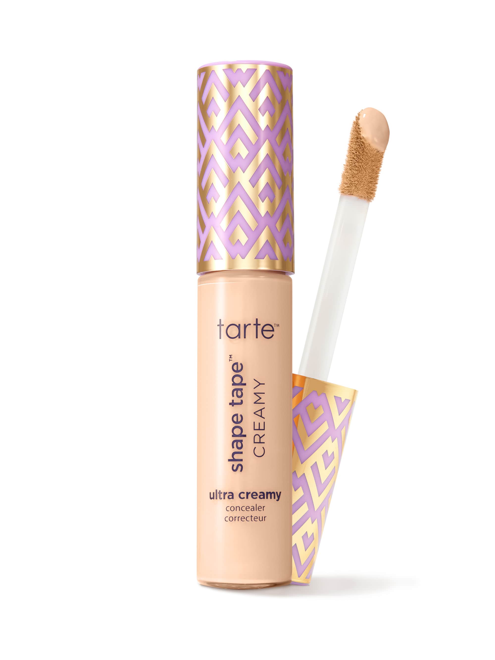A Tarte concealer tube with its wand removed, the applicator showing a beige cream, photographed on a white background. Text on tube: tarte; shape tape™ CREAMY; ultra creamy concealer.